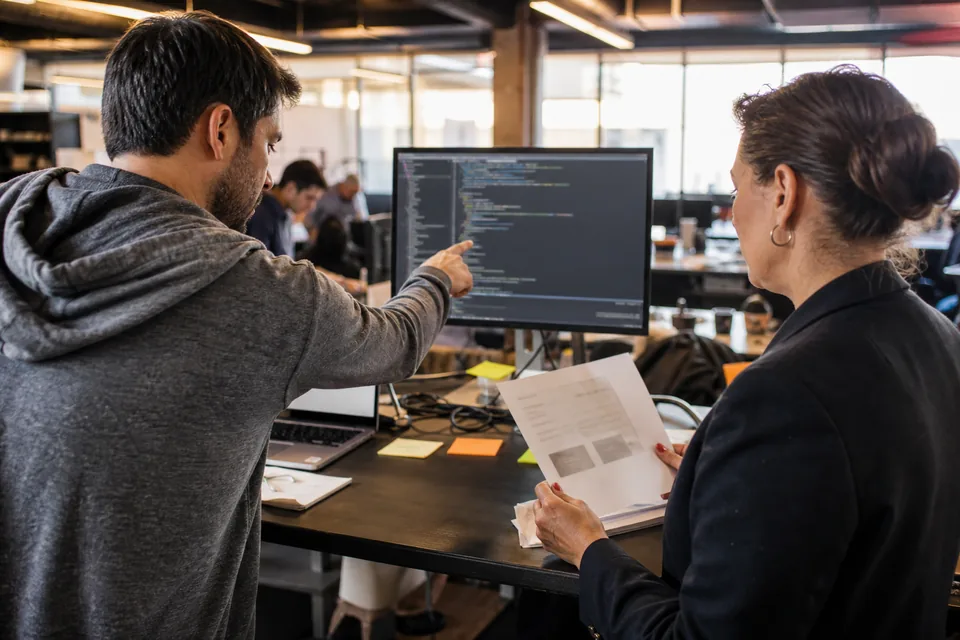 Software engineer and finance lead reviewing API integration costs together at a standing desk