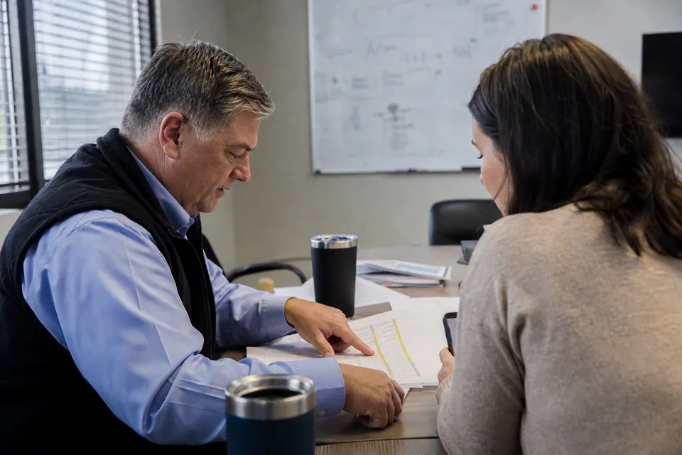 Two finance colleagues reviewing a printed budget report in a small conference room