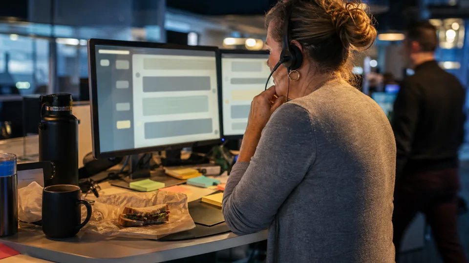 Support agent with a headset reviewing an AI agent conversation handoff at a standing desk