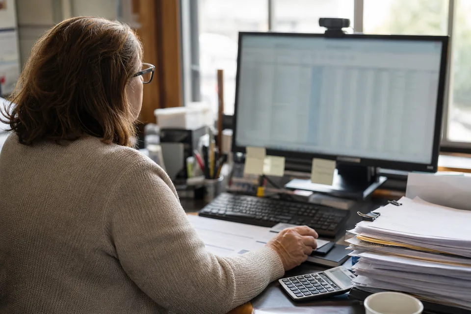 Accounts payable manager at an office desk reviewing a batch of supplier payments on a monitor before approval
